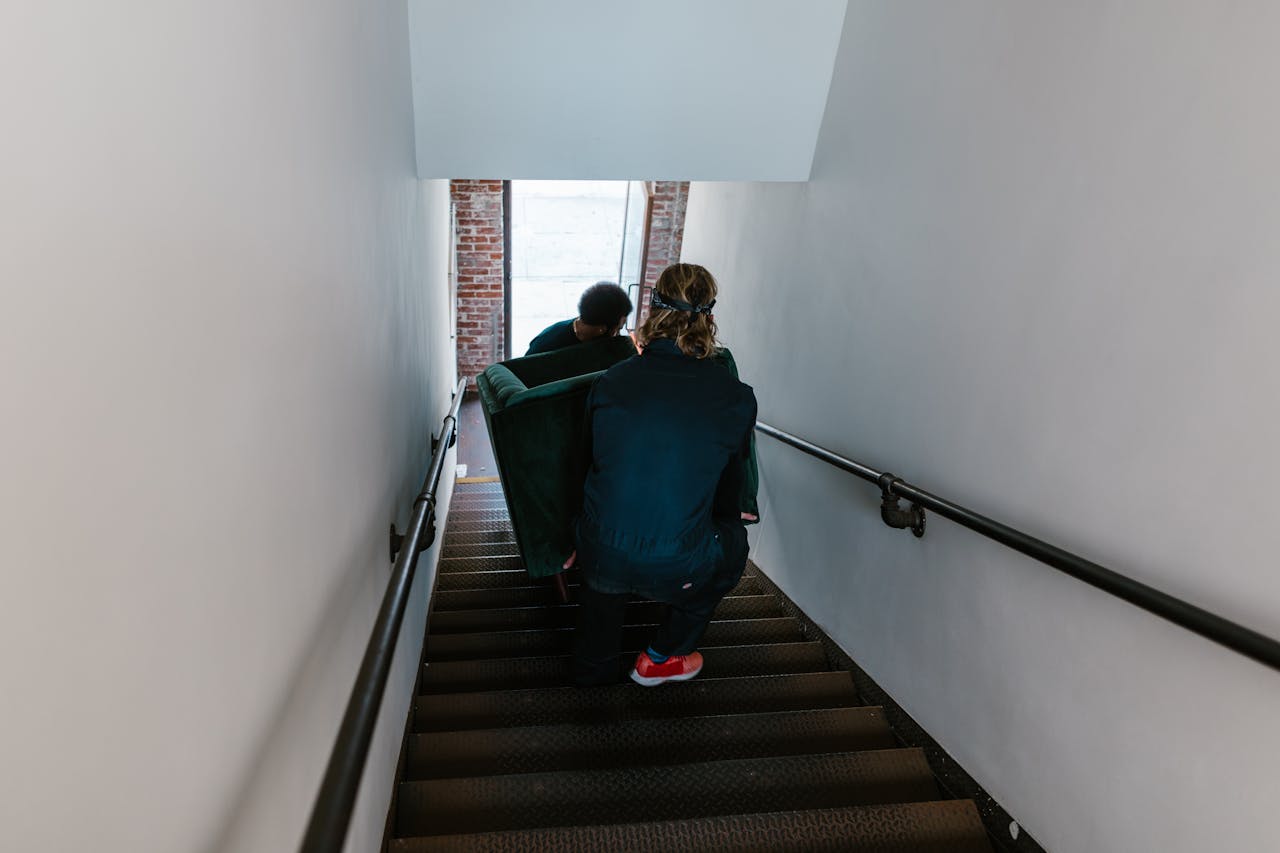 Two men carefully move a couch down a staircase in an indoor setting.