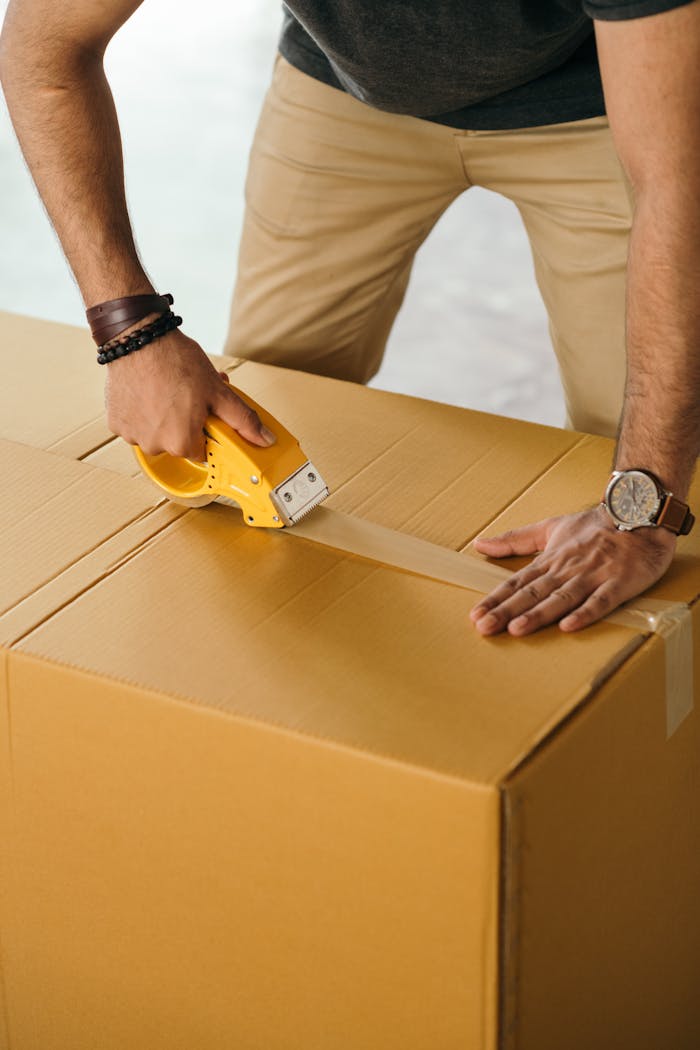Services-03 Unrecognizable man sealing box with duck tape while preparing for moving out
